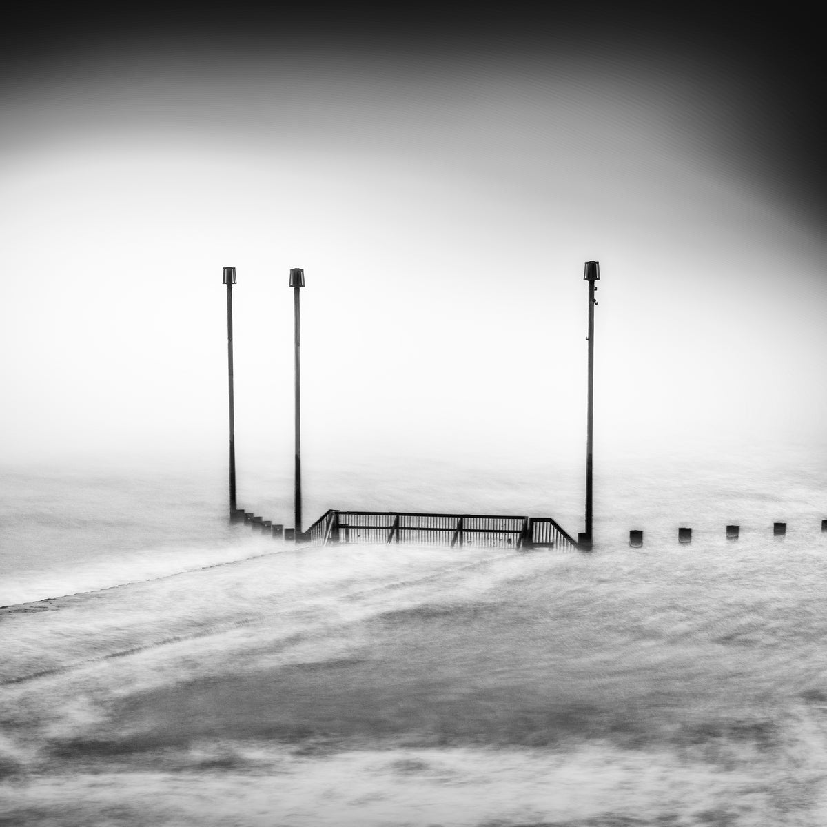 The Remaining, original black-and-white photograph of three upright posts and a railing in pale moving water.